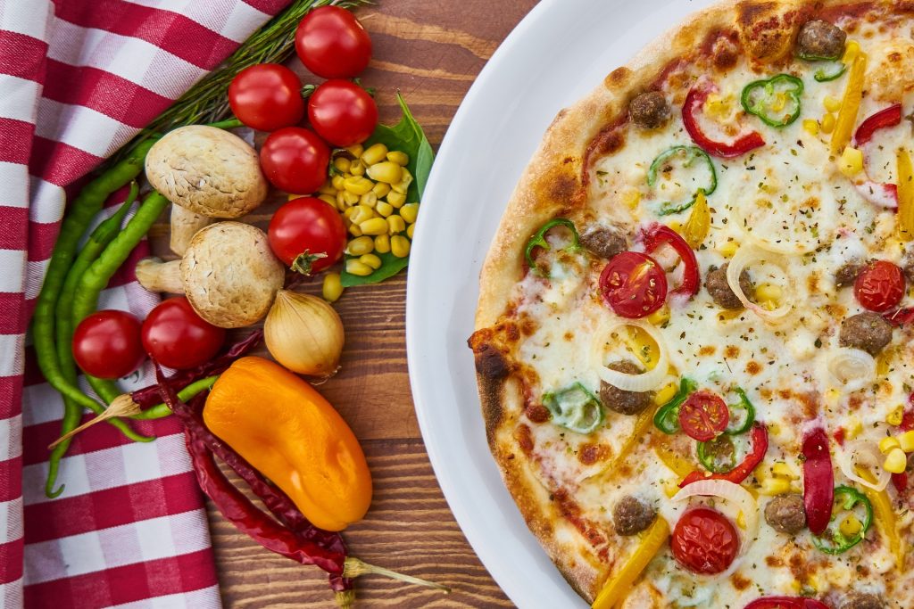 close up ariel view of a pizza where half of it is off the picture; on the left next to the pizza is a variety of whole vegetable.