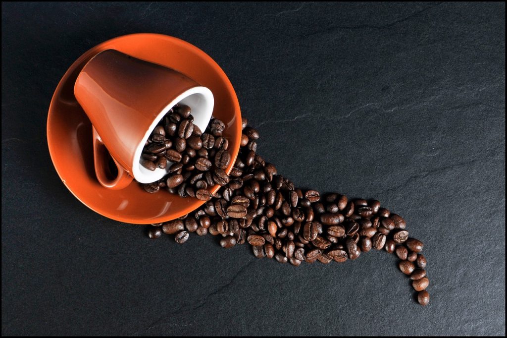 Areal shot of a caramel colored coffee cup on a similar colored cafe plate spilled over with beans flowing out of it in a fluid snake like shape